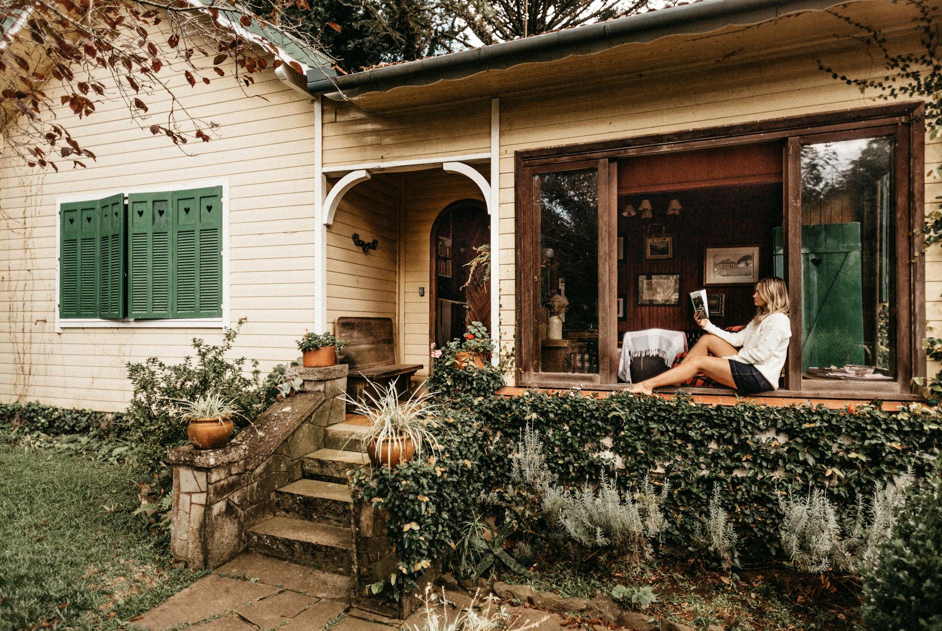 photo of woman sitting on window holding book