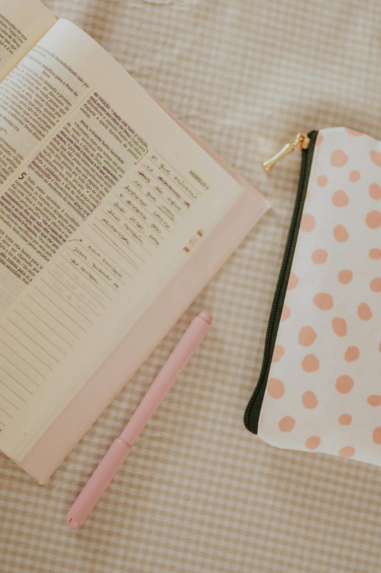 Flat lay of an open Bible with a pink pen and polka dot pouch on a checkered tablecloth.